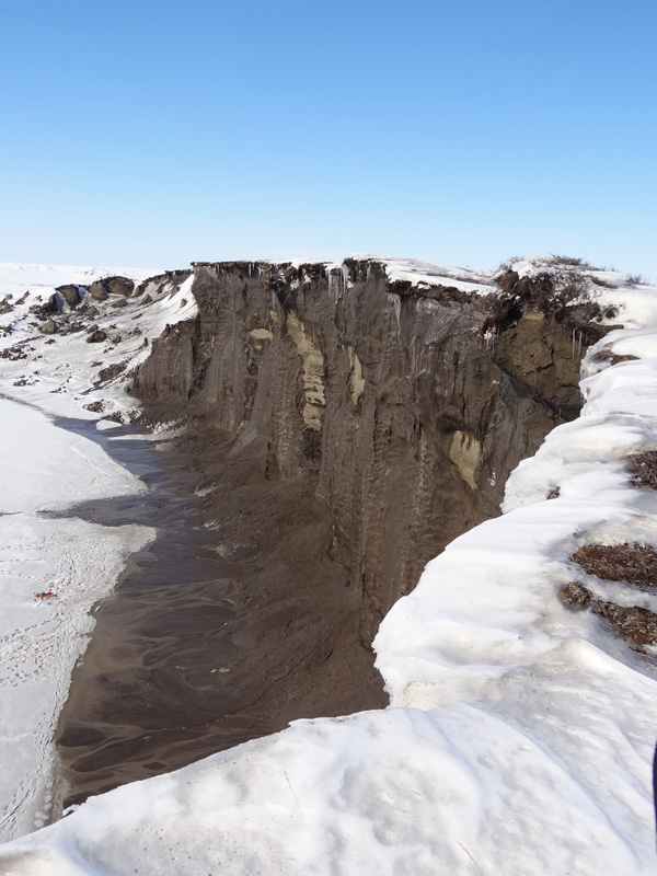 AWI | | JensStrauss | Tauen in der Sommersonne: Blick auf die 35 Meter hohe und 680 Meter lange Steilwand (Permafrost-Aufschluss) am Itkillit River im Norden Alaskas. Obwohl der Fluss oberflächlich noch gefroren ist, rinnen Tauwasserströme die Wand hinab.