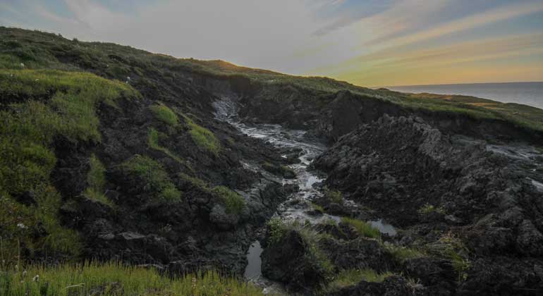 Alfred-Wegener-Institut (AWI) | Jaroslav Obu | By melting processes eroding coastal landscape with meltwater on Herschel Island, Yukon, Canada The Alfred Wegener Institute Helmholtz Center for Polar and Marine Research (AWI) commenced research in the western Canadian Arctic with the funding of the young researcher project titled Coastal Permafrost Erosion (COPER) in 2012. The groupís focus lay on investigating the mass transfer of sediments and carbon across the whole coastal tract of , i.e. include both the emergent and submerged parts of the coast of Herschel Island, Beaufort Sea, Canada. Herschel Island (69.6∞N, 139∞W) is located in the Beaufort Sea, at the northernmost point of the Yukon Territory, and about 70 km east of the Alaskan border. The island is a push-moraine that formed during the westward advance of of the Laurentide Ice Sheet. The coast is characterized by high cliffs and numerous retrogressive thaw slumps, indicating the presence of large massive ice bodies susceptible to permafrost degradation. The tundra covered island is located where mean annual temperatures are well below 0∞C, and rise above freezing only between June and September. Cold temperatures affect coastal processes, as well. Wave- and tide induced processes are limited by the presence of sea ice and landfast ice. The presence of ice, however, introduces some physical processes unique to cold environments such as ice gouging, ice rafting, ice push-up, and ice pile-up. Ice gouging refers to the grounding of ice keels; ice rafting the transport of coarse sediment offshore incorporated into the ice matrix; while ice push-up and pile-up occur at the land-sea boundary, transporting sediments on- and across shore. Coastal erosion is limited to the period of open water. Average rates of erosion are 1-2 m/yr, and may reach 10-30 m/yr.