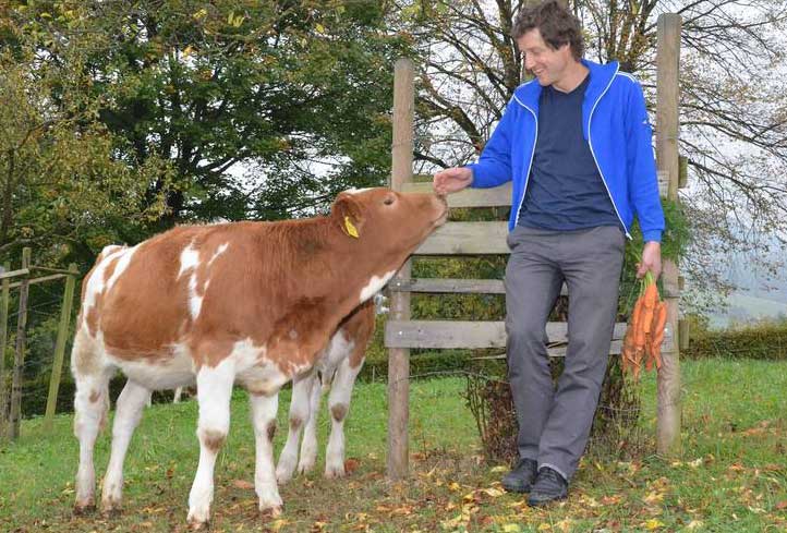 FiBL, Franziska Hämmerli | Organic agriculture has many positive effects on the environment and contributes to solving the problem of the world food supply: This is shown in a new FiBL study. One of the authors, Adrian Müller, is shown on a meadow with an organic calf and organic carrots.