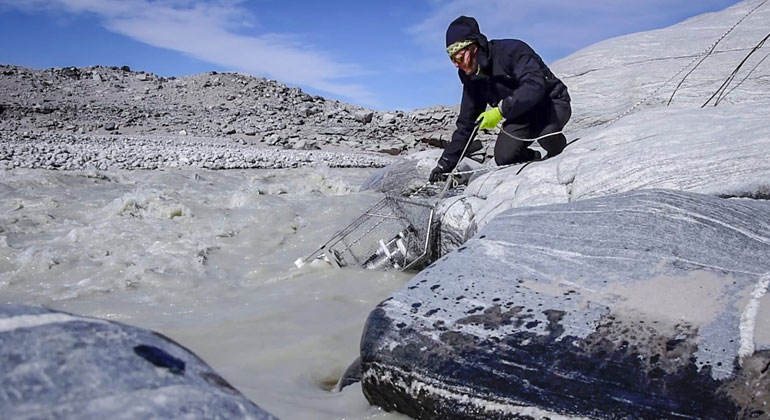 University of Bristol | Marie Bulinova | Guillaume Lamarche-Gagnon sampling some water with a syringe into a vial for later methane analysis, with the Glacier visible in the background.